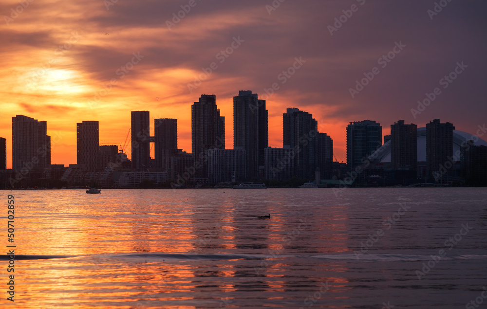 Summer sunset view from Toronto Islands across the Inner Harbour of the Lake Ontario on Downtown Toronto skyline with skyscrapers under a magnificent sky
