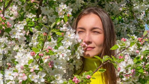 Portrait of beautiful young woman in apple trees blooming park on a sunny day. Smiling girl with apple trees flowers.