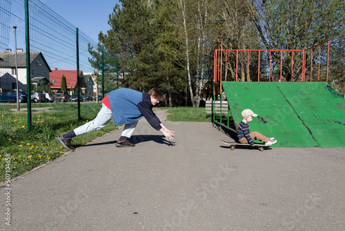 The older brother patiently and lovingly teaches the little boy his favorite hobby - to skate on a playground in the park in the fresh air. photo