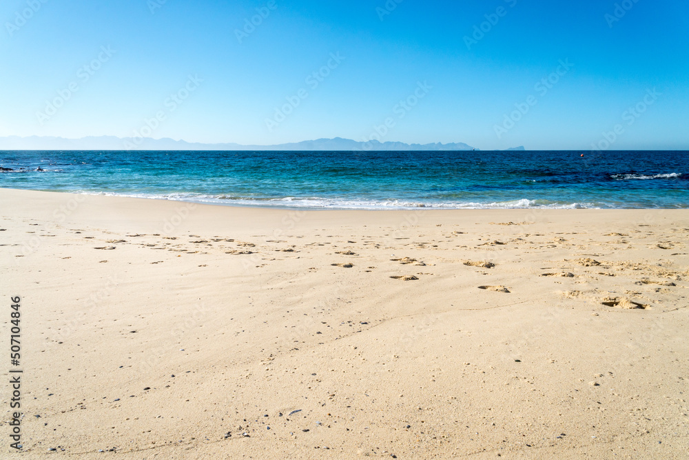 white sand beach and sea with mountains in the background on a sunny cloudless day with blue sky seascape or landscape