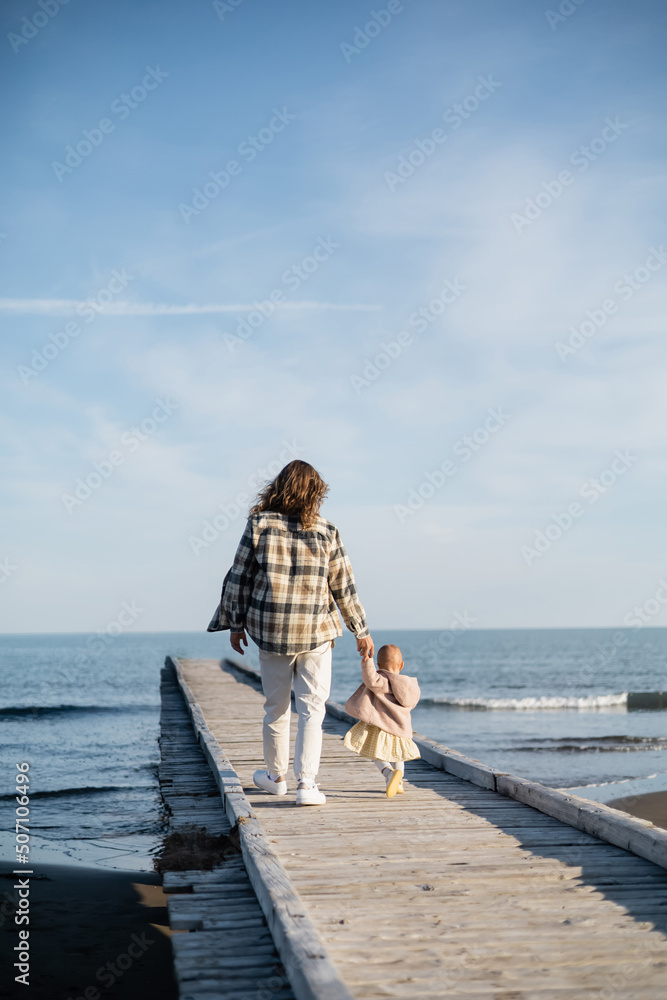 Back view of father and baby girl walking on pier near adriatic sea in Italy.