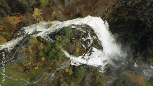 Aerial view of the Skjerfossen waterfall. A powerful stream of whitewater falls from the forest-covered cliffs. A narrow hiking trail winds on the slope. photo