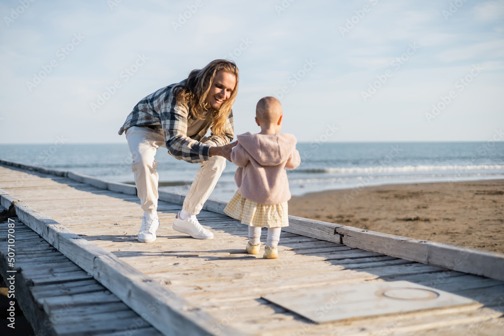 Positive man in shirt looking away baby on wooden pier in Italy.
