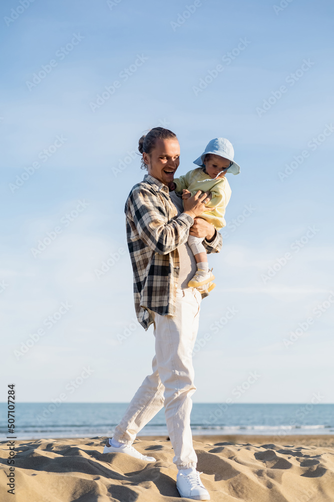 Positive father holding toddler child walking walking on beach in Treviso.