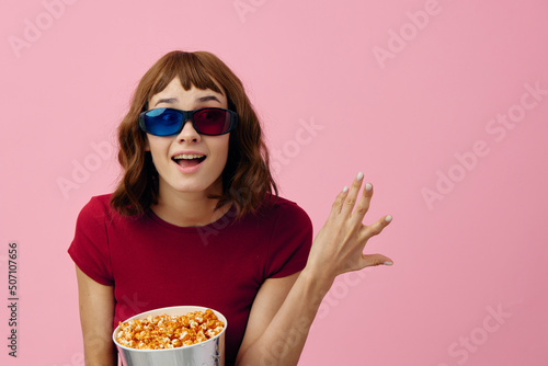 Overjoyed happy cute redhead lady in red t-shirt 3D glasses with popcorn watch movie posing isolated on over pink studio background. Copy space Banner. Fashion Cinema concept. Entertainment offer