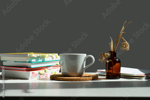 a stack of books on a table with a mug of cha and a vase of dried flowers. photo