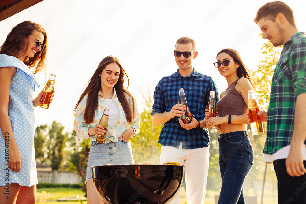 Friends have a barbecue party outdoors during outdoor recreation. Group of friends drink drinks and eat grilled