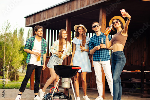 group of cheerful young friends having a barbecue party in the backyard, taking a selfie on a mobile phone photo