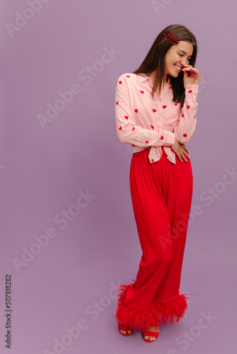 Full-length pretty young caucasian girl laughs away on purple background with place for text. Brunette girl wears blouse, pants and shoes to meeting. People's emotions, lifestyle and fashion concept.  photo