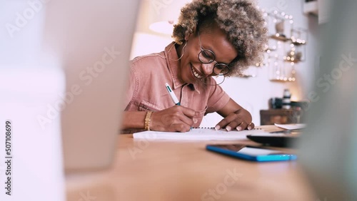 Afro woman writing in a notebook at home on an office table.