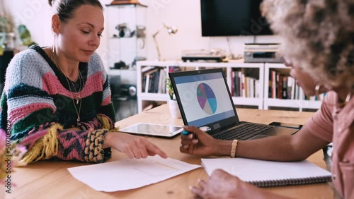 Two business women sitting at table in office discuss topics.