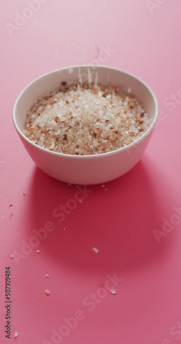 Vertical image of flavoured salt crystals falling into bowl on pink background
