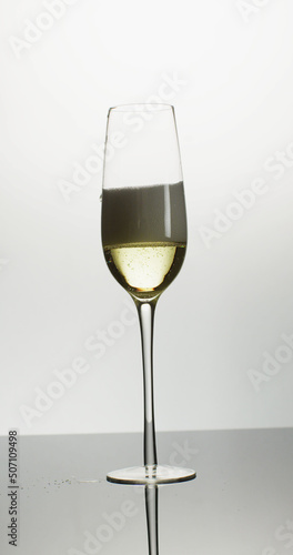 Vertical image of open bottle pouring champagne into single tulip glass on white background