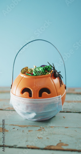 Vertical image of halloween pumpkins basket filled with candy wearing face mask on blue background