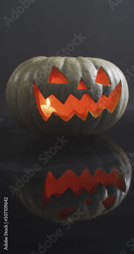 Vertical image of close of lit carved halloween pumpkin on grey background