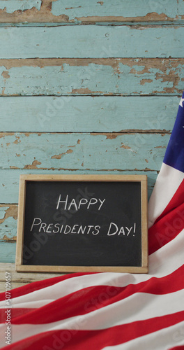Vertical image of happy presidents day text on chalkboard with american flag against painted boards