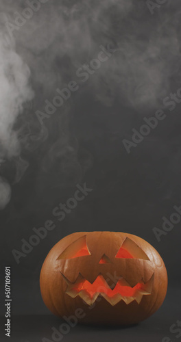 Vertical image of lit carved halloween pumpkins with clouds of smoke on grey background