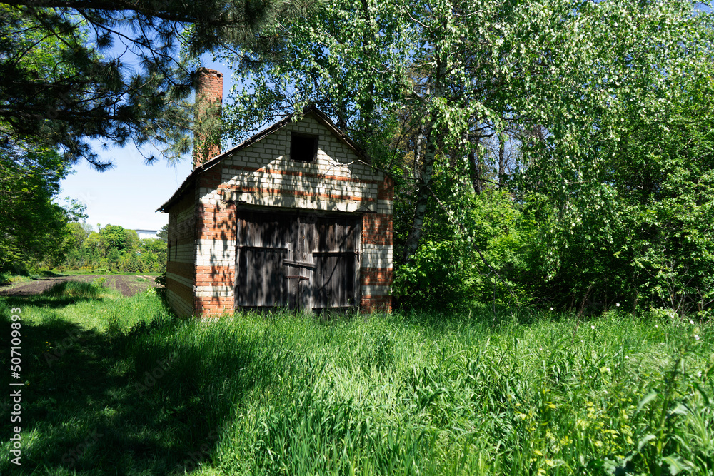 An abandoned brick house in the forest with a large gate in sunny weather An abandoned brick house in the forest with a large gate in sunny weather