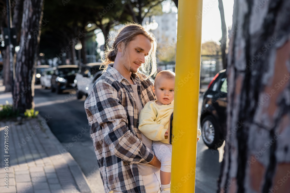 Young man holding baby girl near road on urban street in Treviso.