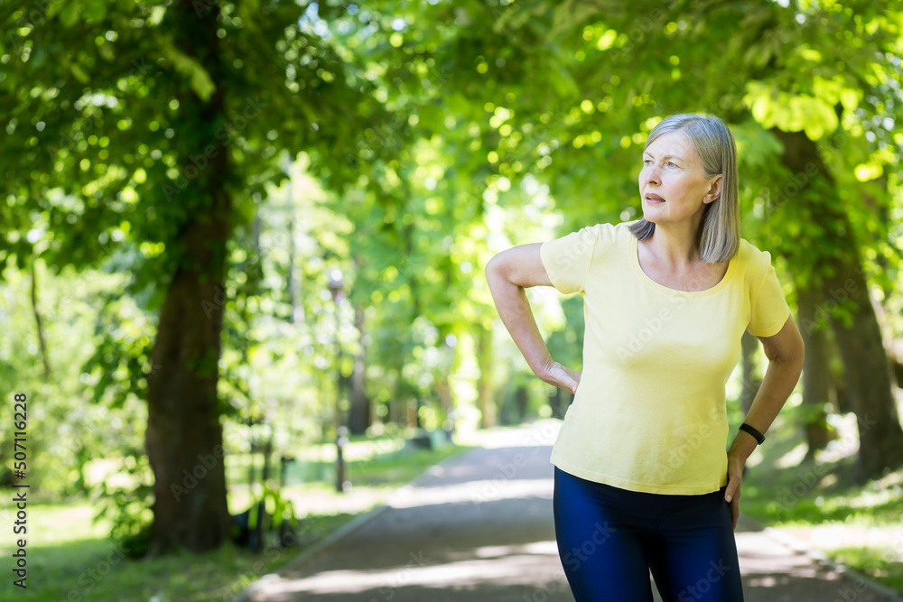 Senior active woman on a walk in the park injured her back, pensioner on a jog on a summer day