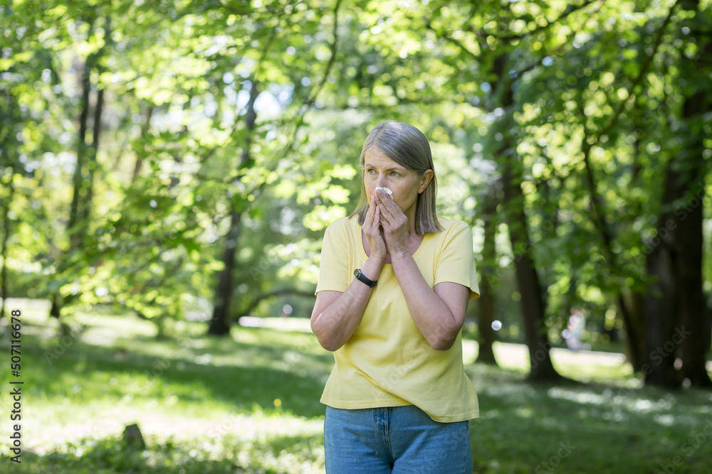 An elderly woman in the park with allergies has a runny nose and sneezes near trees An elderly woman in the park with allergies has a runny nose and sneezes near trees