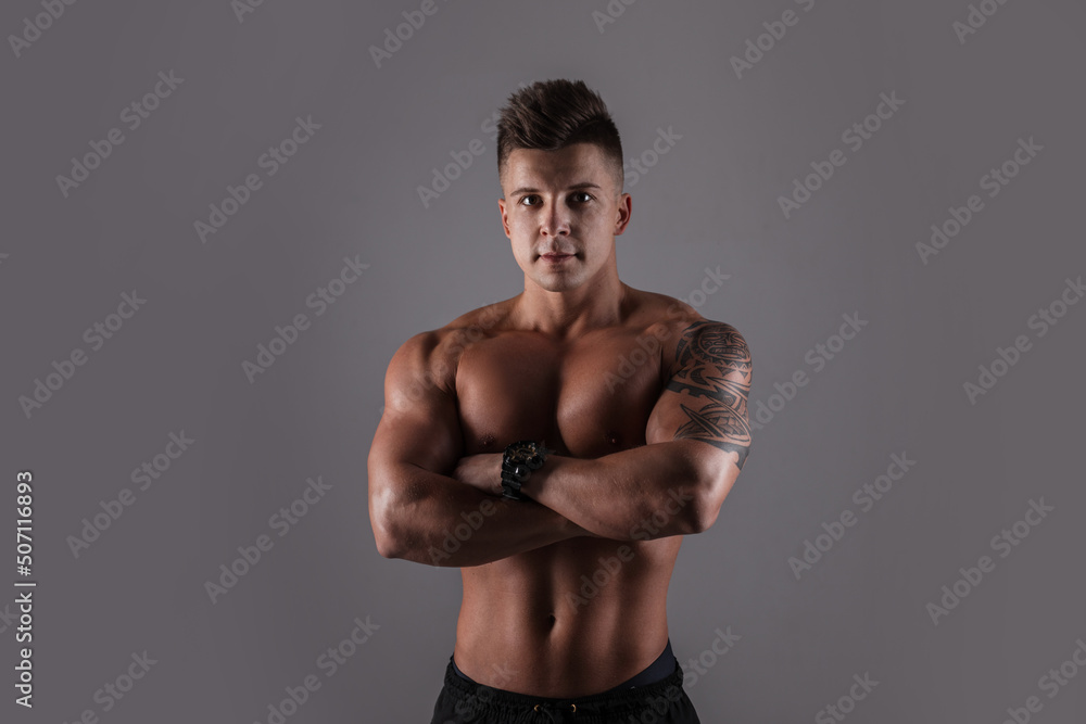 Fototapeta premium Fashionable handsome athletic bodybuilder guy with hair with a muscular naked body in a studio on a dark background. Men's portrait of a healthy man