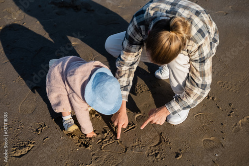 Overhead view of man and baby girl drawing on beach.