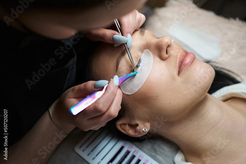eyelash extension master doing eyelash extension procedure to young woman with dark hair