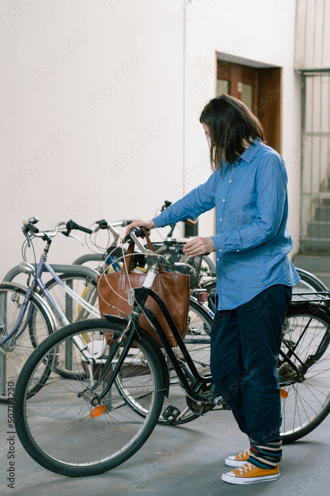 Fototapeta premium Woman with a blue shirt and yellow sneakers parking her black urban bicycle in a bike parking.