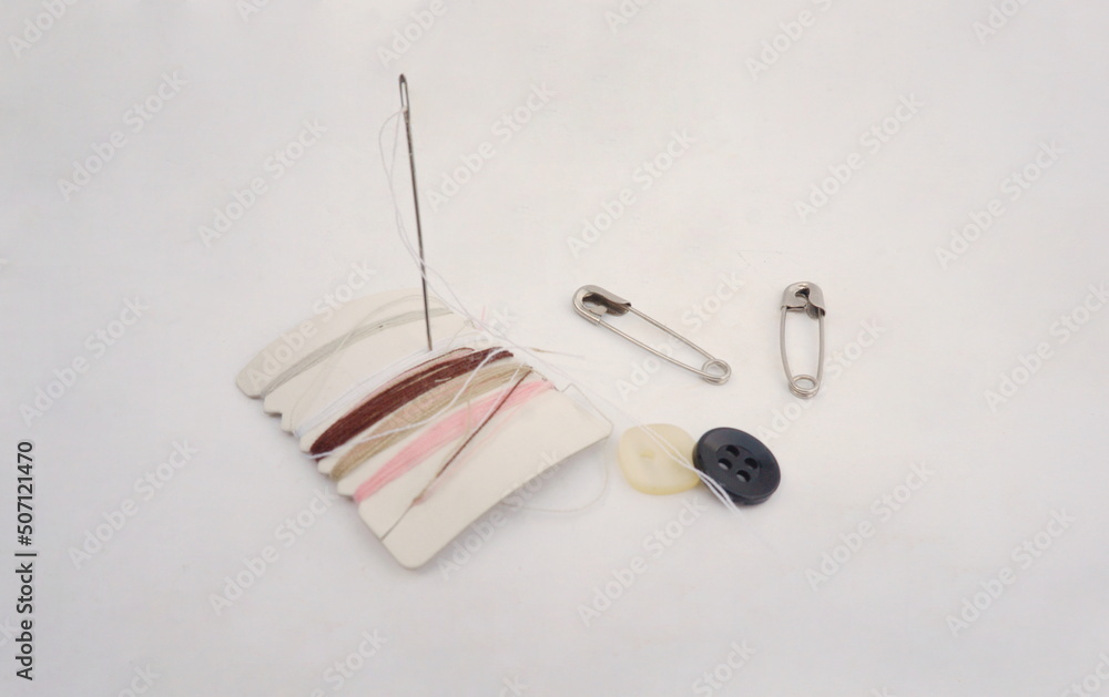 Sewing Kit wtih Pink, Tan, White, Gray, Brown Threads, Needle, Two Buttons and Saftey Pins on White Background with Room for Text