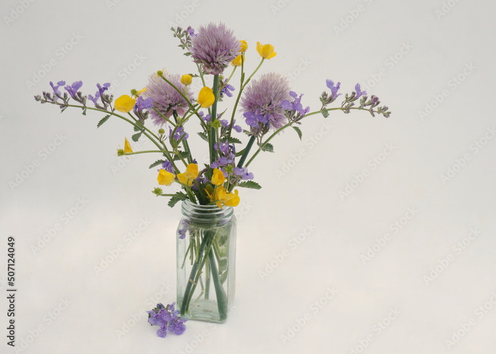 Purple and Yellow Wildflowers in Glass Bottle on White Background