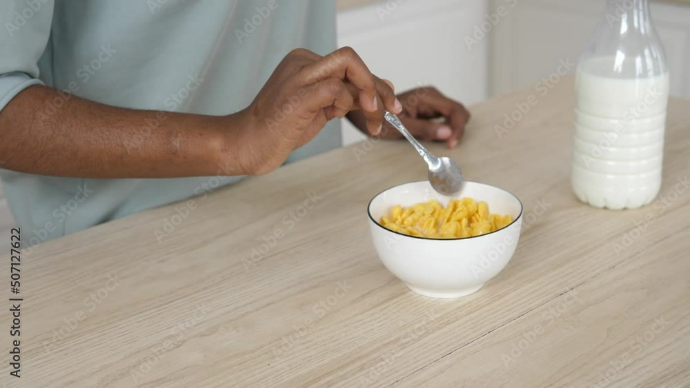 Close-up of the hand of a dark-skinned girl stirs crispy muesli with milk in a bowl, in slow motion. Healthy quick breakfast Close-up of the hand of a dark-skinned girl stirs crispy muesli with milk in a bowl, in slow motion. Healthy quick breakfast