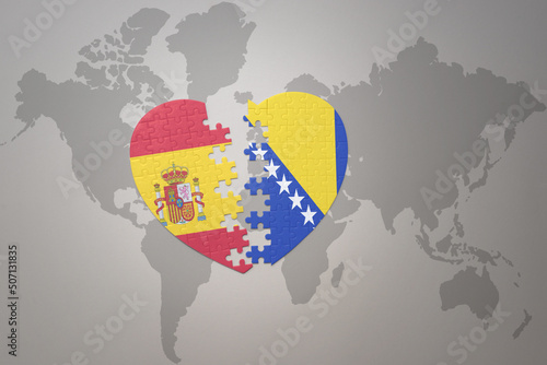 puzzle heart with the national flag of bosnia and herzegovina and spain on a world map background. Concept.