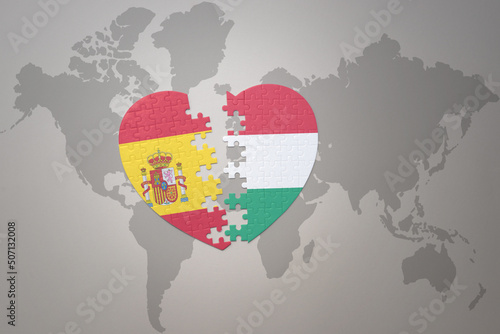 puzzle heart with the national flag of hungary and spain on a world map background. Concept.