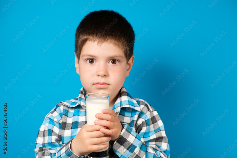 A 4-year-old boy holds a glass of milk on a blue background. The benefits and harms of milk for preschool children. A 4-year-old boy holds a glass of milk on a blue background. The benefits and harms of milk for preschool children.