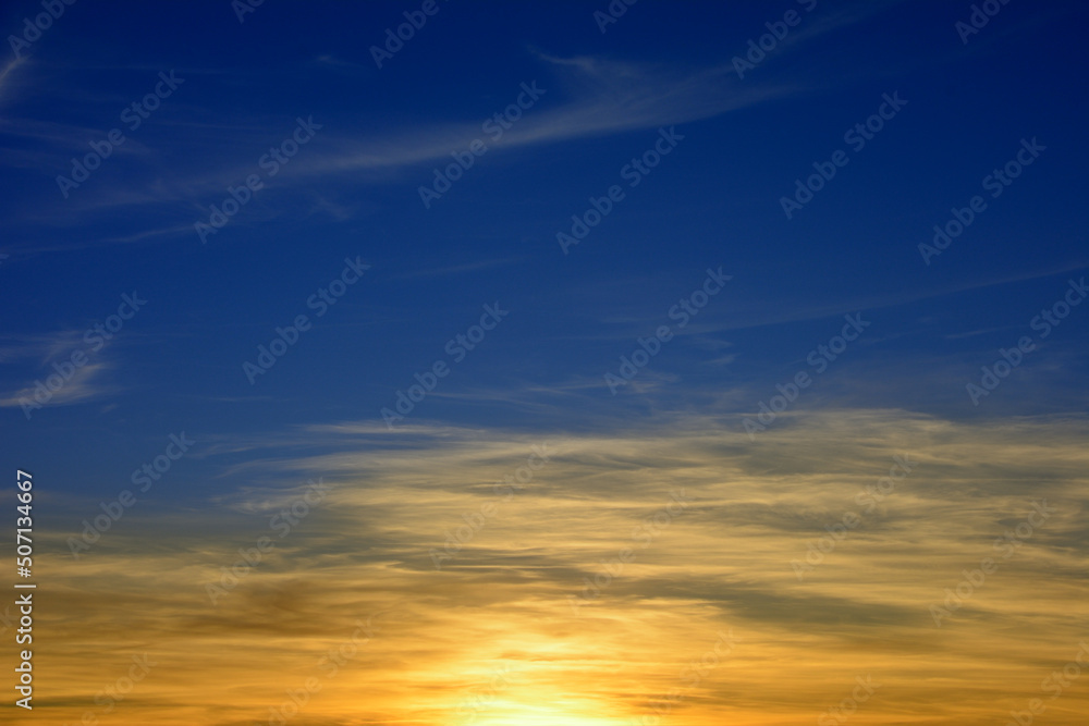 Dark blue evening sky with sun rays at sunset and illuminated clouds