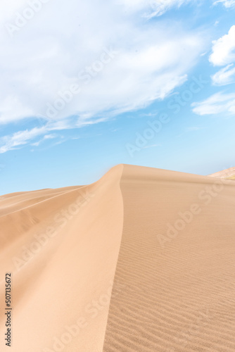 Vertical view of a large sand dune with blue sky in the back and some clouds.