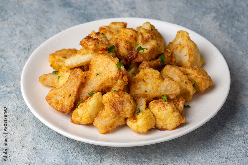 Fried in batter Cauliflower florets served on a black plate on a grey concrete table with ingredients, view from above, close-up, flatlay, copy space Fried in batter Cauliflower florets served on a black plate on a grey concrete table with ingredients, view from above, close-up, flatlay, copy space
