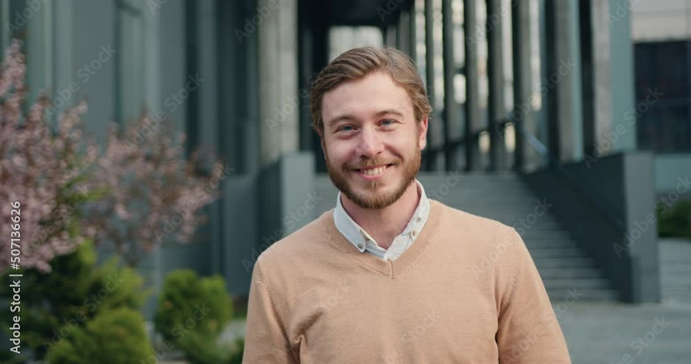 Close-up portrait of handsome success man, looking up at camera, smiling at office building background. Outdoors Close-up portrait of handsome success man, looking up at camera, smiling at office building background. Outdoors