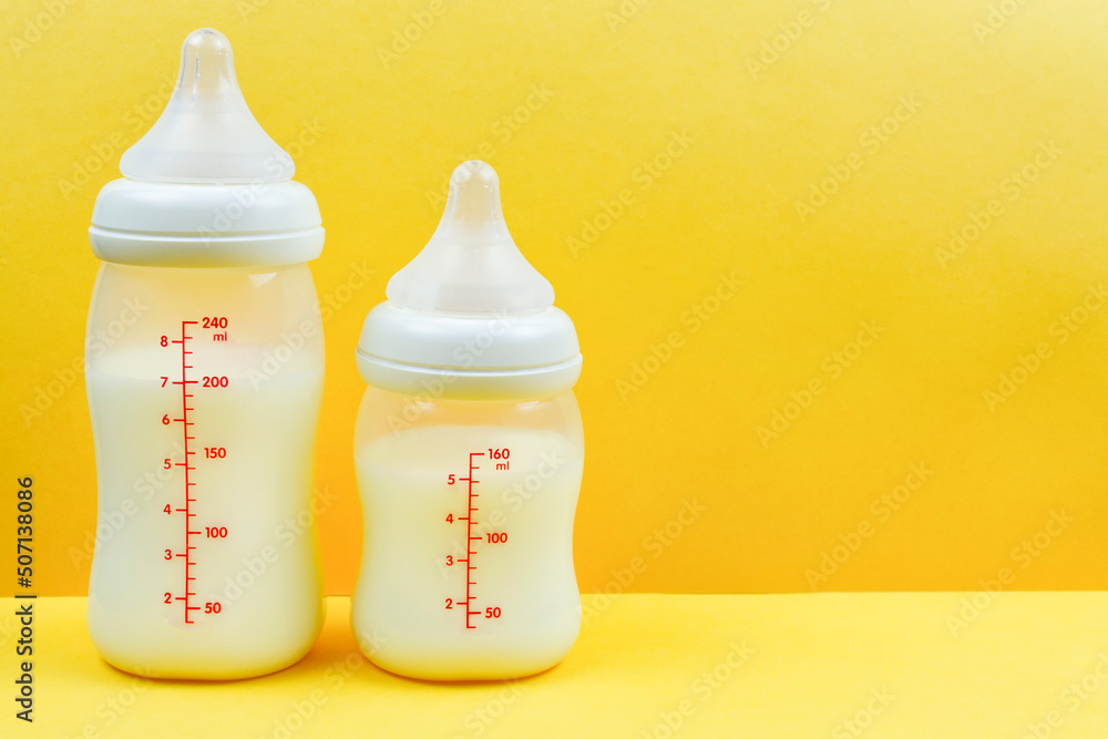 Two baby bottles with milk formula on a bright yellow background. Space for the text. Artificial feeding of the baby.