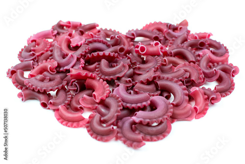 Dry colored Italian pasta creste di galli in the shape of a heart on a white isolated background. Pasta with beetroot in burgundy color.