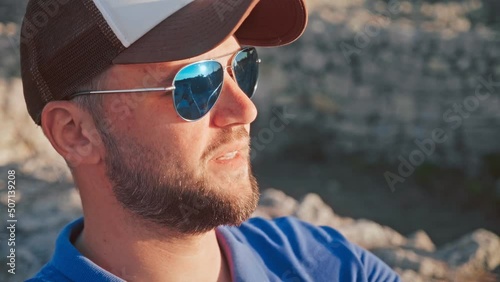 Close-up portrait of Young man in white baseball cap taking selfie on smartphone against the background of old historical stone walls. A round-the-world trip to historical places. Summer vacation photo