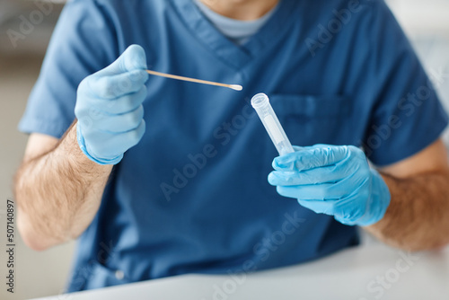 Unrecognizable medical worker wearing protective latex gloves taking out stick from tube to do swab test