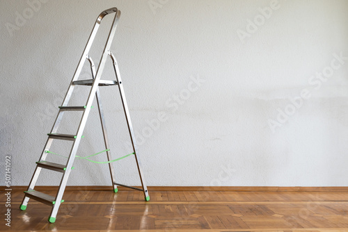 Foldable chrome stepladder against blank wall indoors