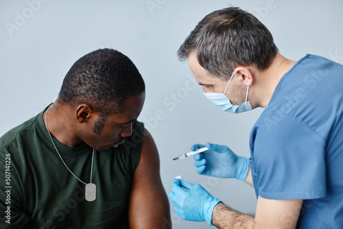 Modern young African American military officer getting vaccine injection into shoulder to prevent coronavirus