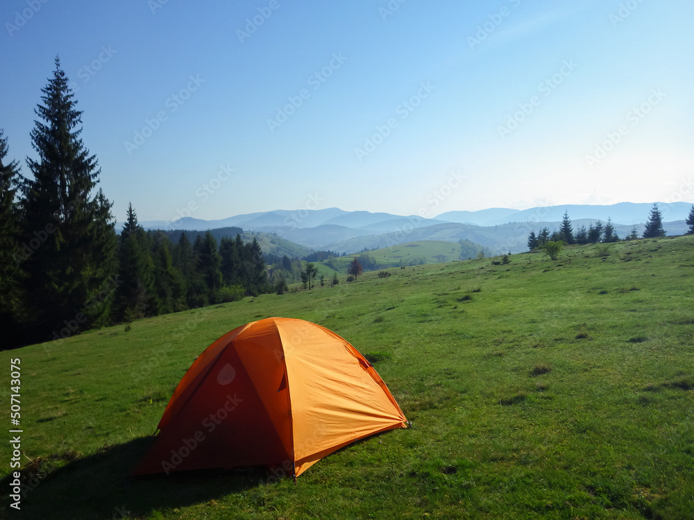orange tourist tent on a mountain meadow in the Carpathian mountains