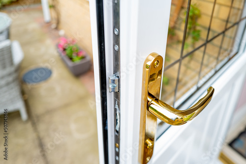 Shallow focus of the brass coloured door handle on a newly installed double glazed door. Showing the leaded window, leading out onto a patio area