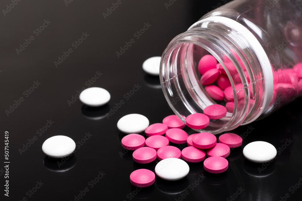 Pink and white pills with a bottle on a black background Pink and white pills with a bottle on a black background