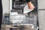 A women's hands load dishes into an open dishwasher in a modern bright kitchen. The concept of household home life
