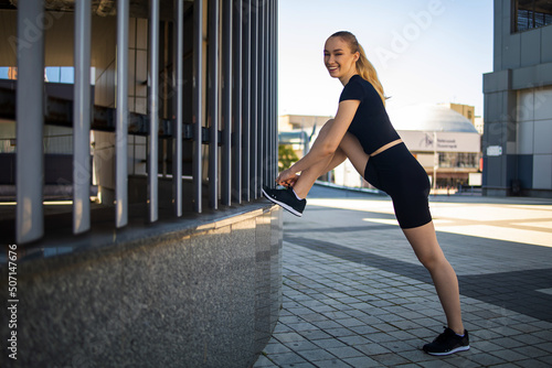 Fitness runner body close up, woman doing warm-up before jogging, stretching leg muscles, Female athlete prepares legs for cardio workout, outdoor exercise in city.